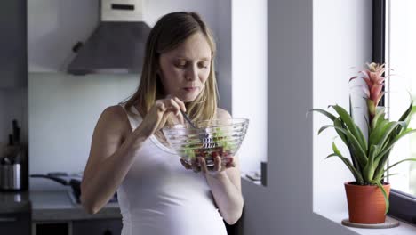 Cheerful-pregnant-woman-eating-healthy-food-at-kitchen